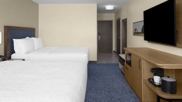 Hotelkamer met twee bedden, een televisie, een bureau met koffiezetapparaat en een deur naar een gang.