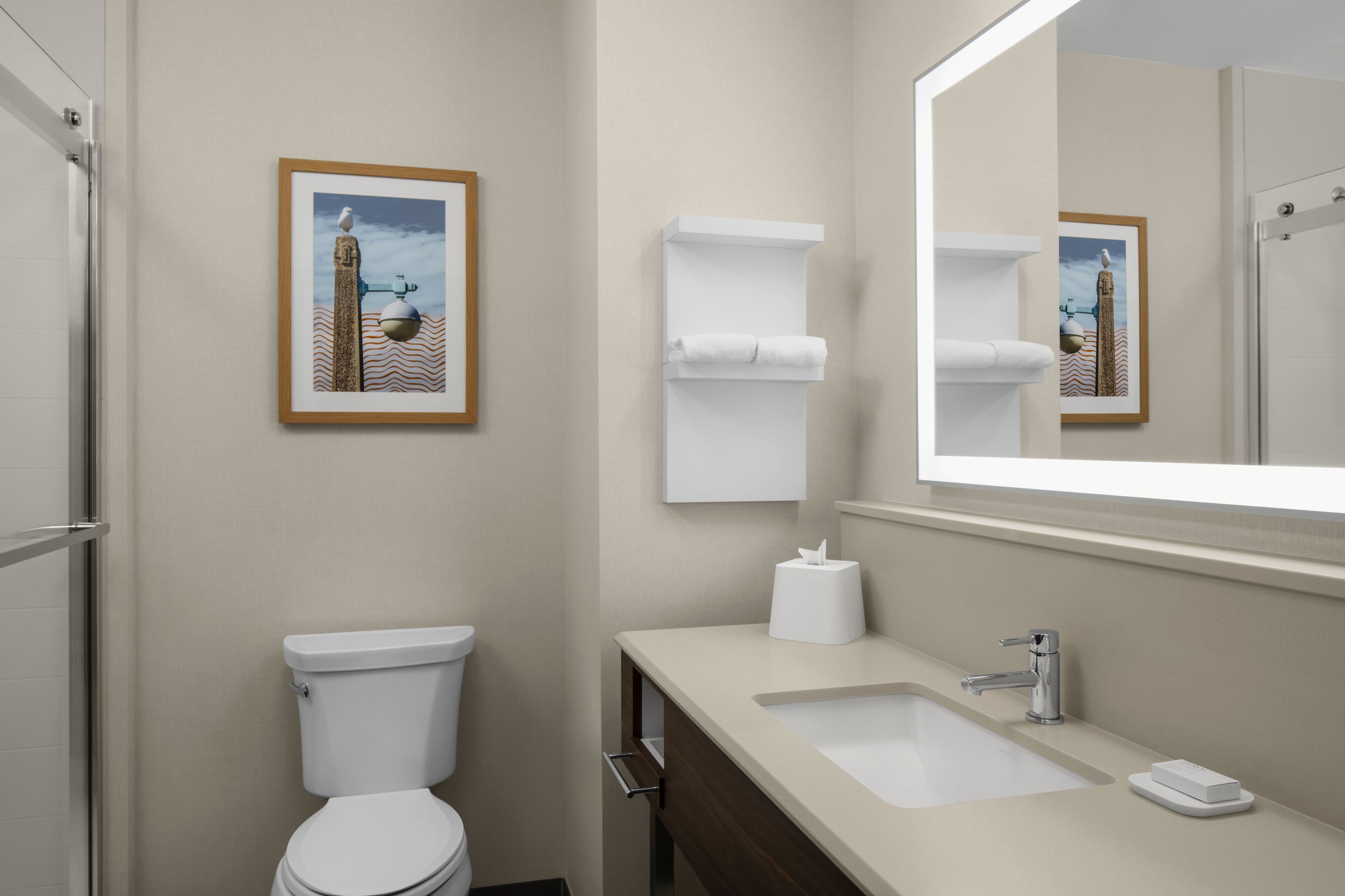 A modern bathroom with a toilet, sink, and mirror. There are framed pictures on the wall and a towel rack.