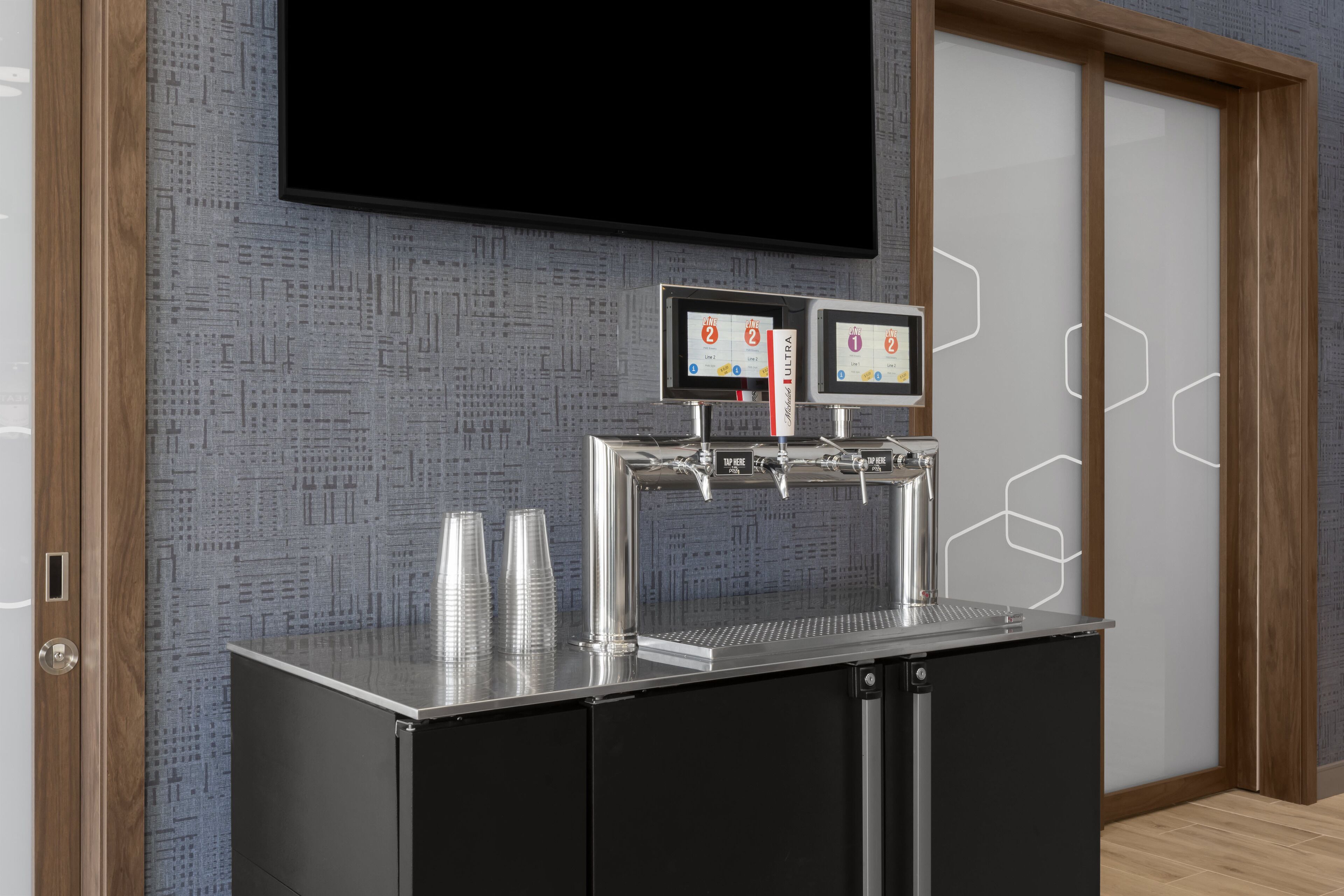 Un angolo bevande self-service con due erogatori, una TV a schermo piatto montata sopra e una parete decorata sullo sfondo.