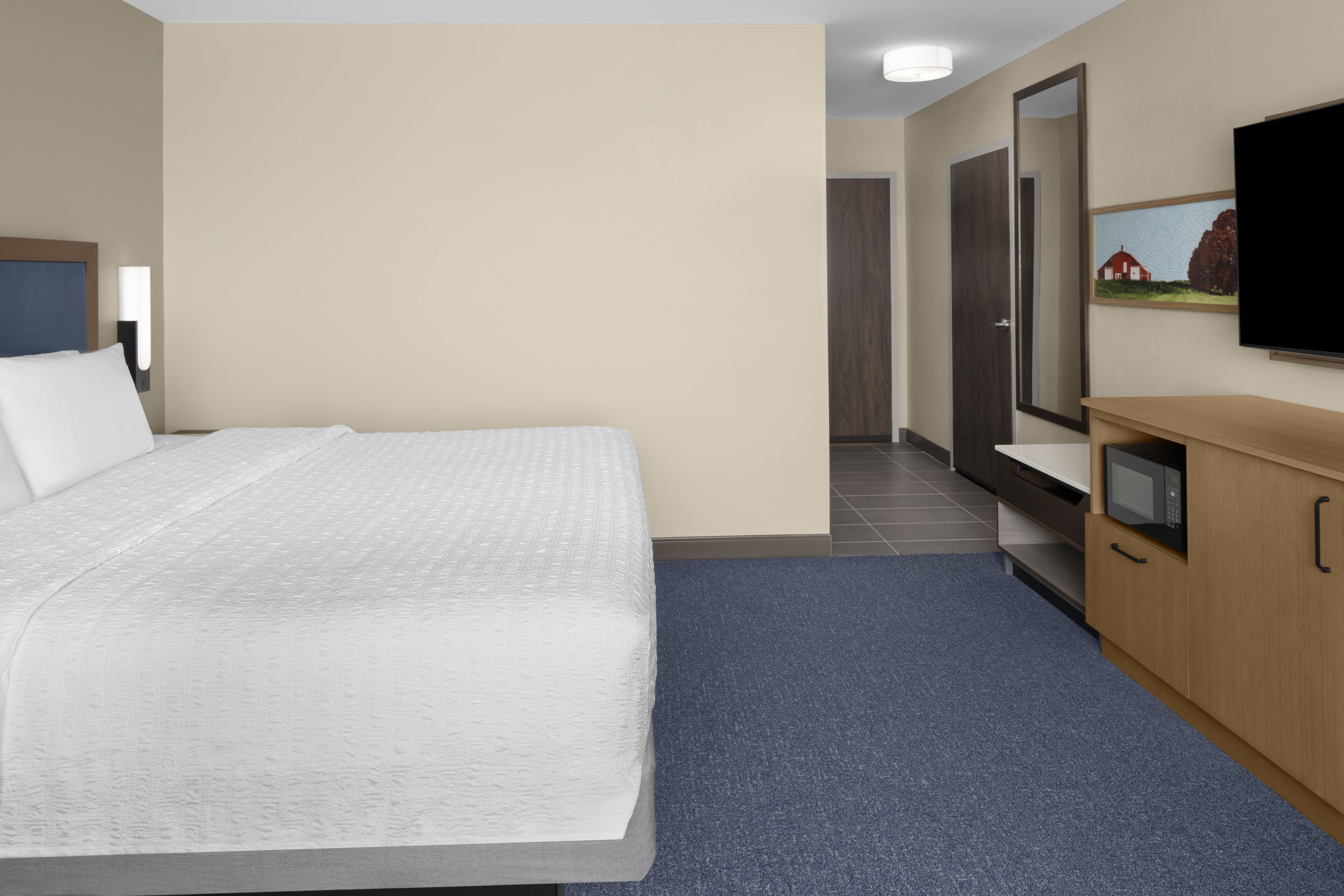 A hotel room with a bed, a TV, a wooden dresser, and a door leading to a bathroom.