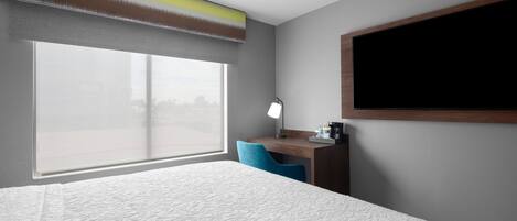 Een hotelkamer met een groot raam, een bureau met een lamp en een bed met een geribbelde matras.