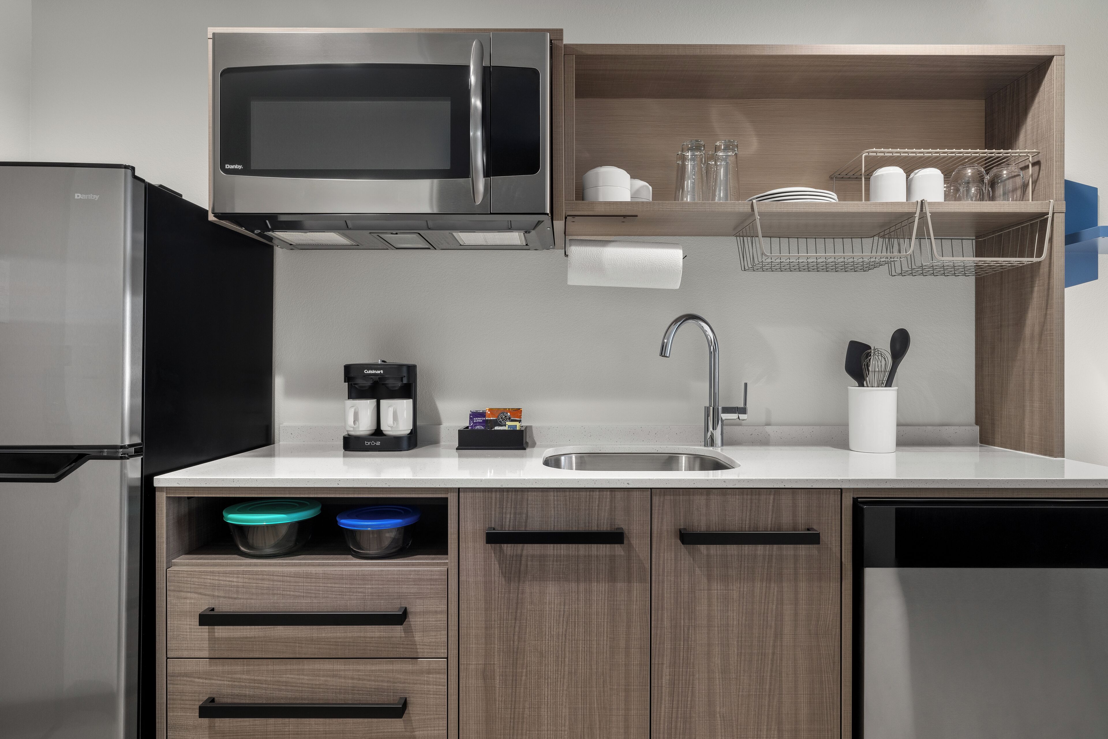 A modern kitchen with a stainless steel refrigerator, a built-in microwave, a coffee maker, and a sink.