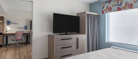 A hotel room with a bed, a desk with a chair, a television on a cabinet, and a window with curtains.