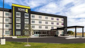 Un hotel moderno con un cartello ben visibile 'HOME 2', diversi piani e una zona esterna coperta con posti a sedere.