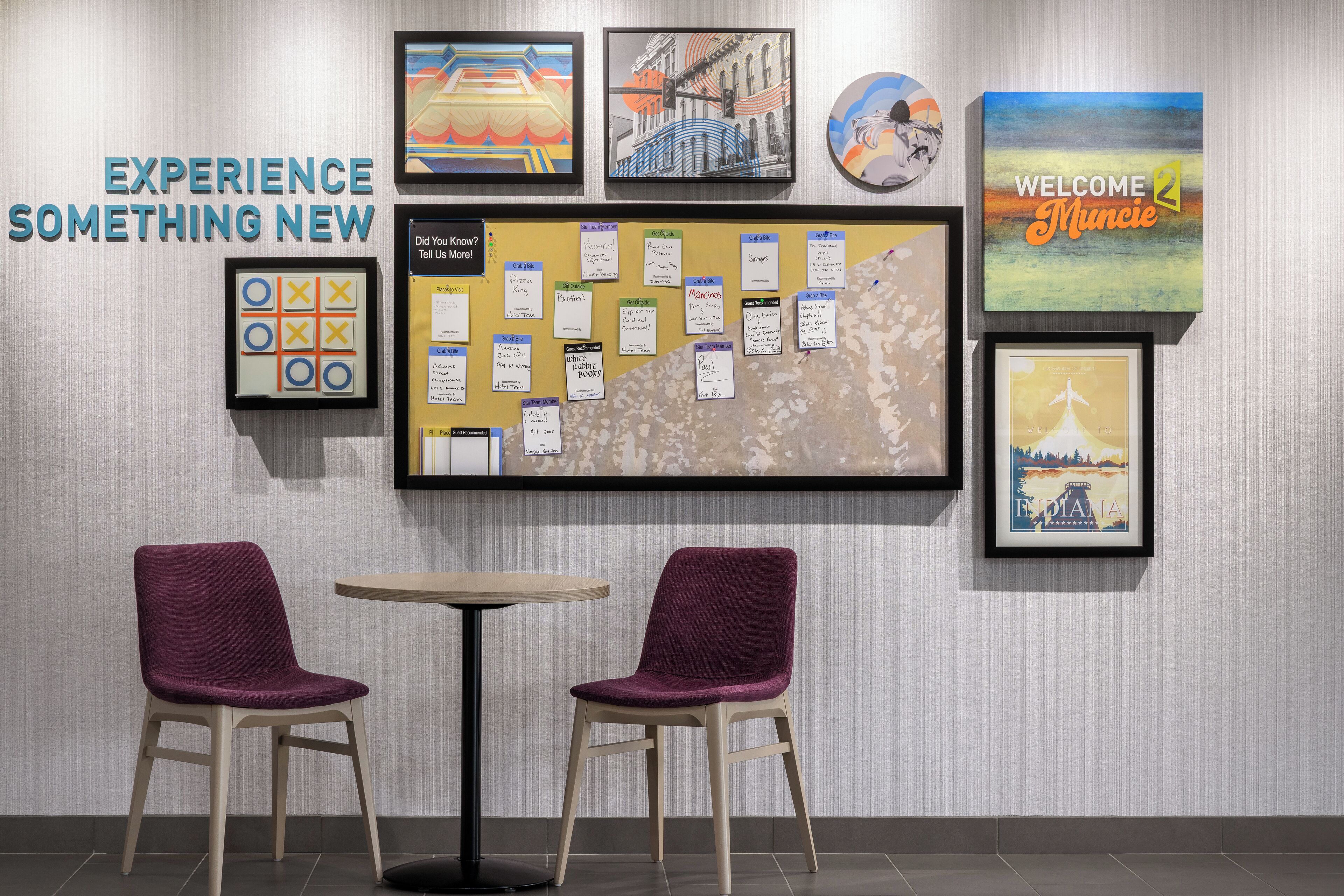 A wall with framed artwork, a bulletin board with notes, and two purple chairs.