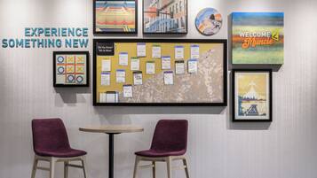 A wall with framed artwork, a bulletin board with notes, and two purple chairs.