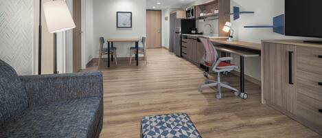 A modern, compact living space with a sofa, a dining table, a kitchen area, and a television.
