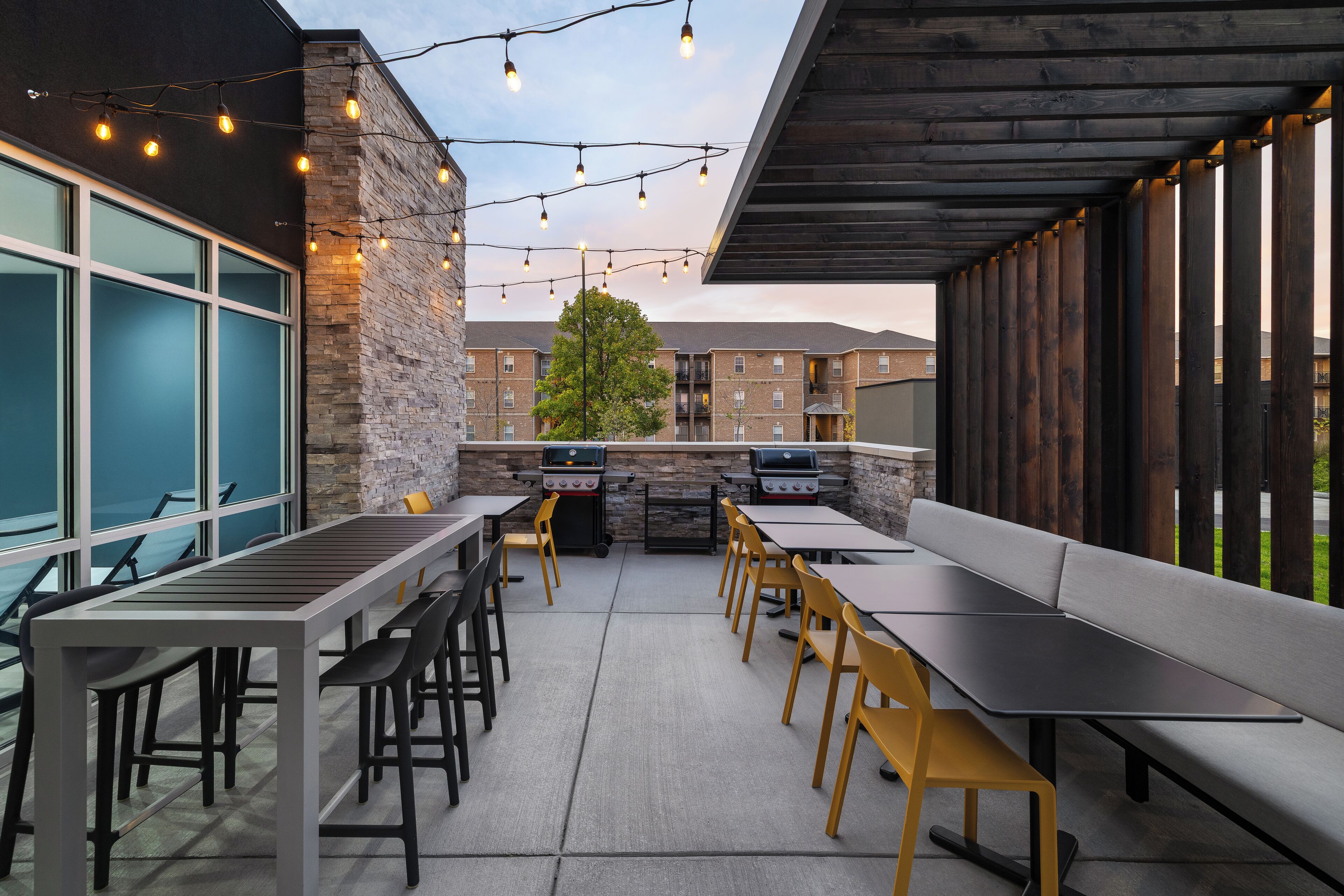An outdoor patio with tables and chairs, string lights, and a brick wall.