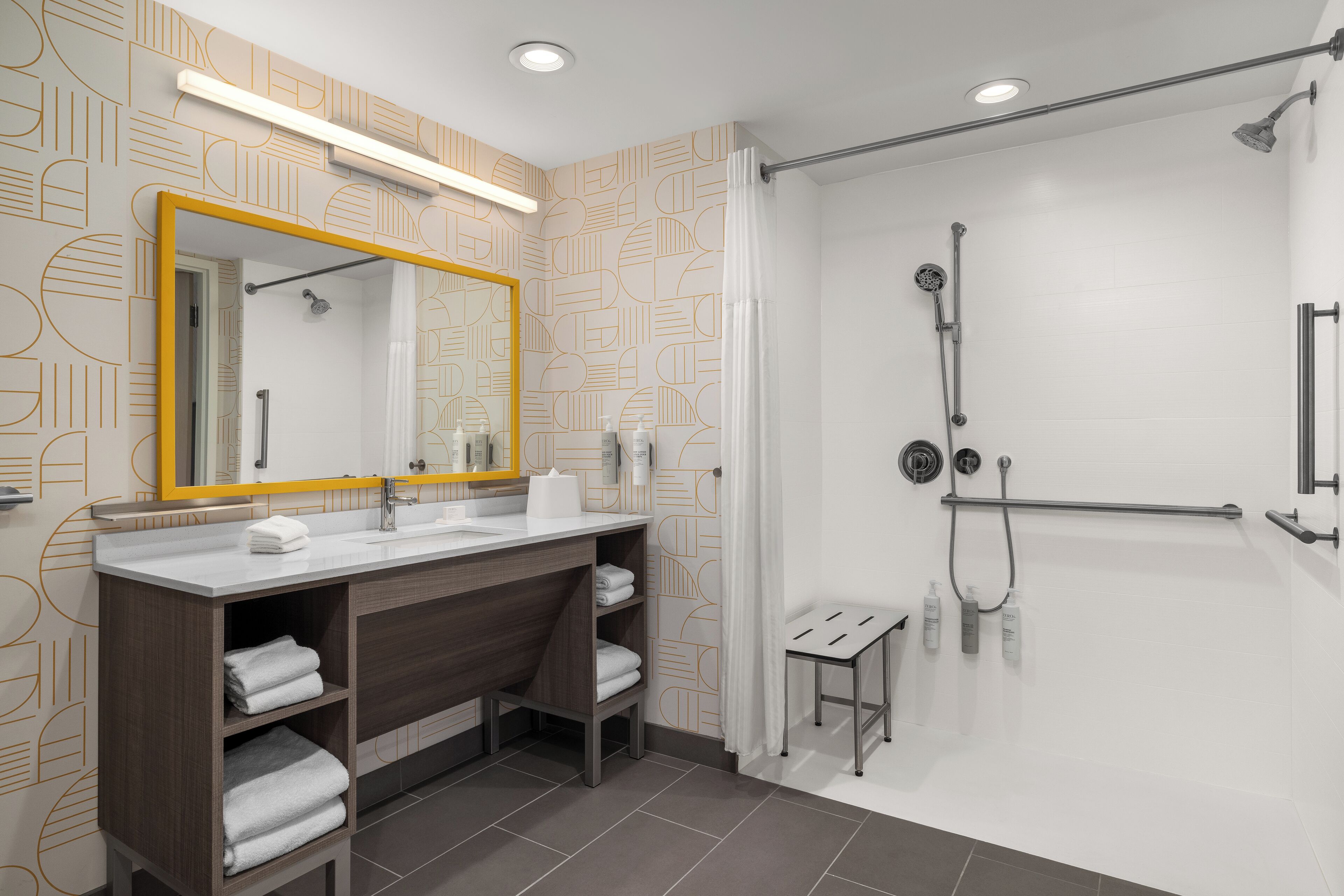 A modern bathroom with a large mirror, two sinks, a shower area, and a small stool.