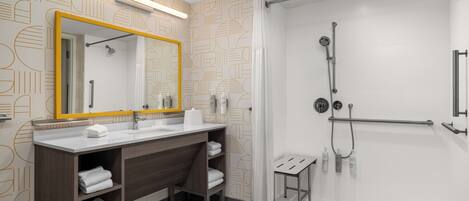 A modern bathroom with a large mirror, two sinks, a shower area, and a small stool.