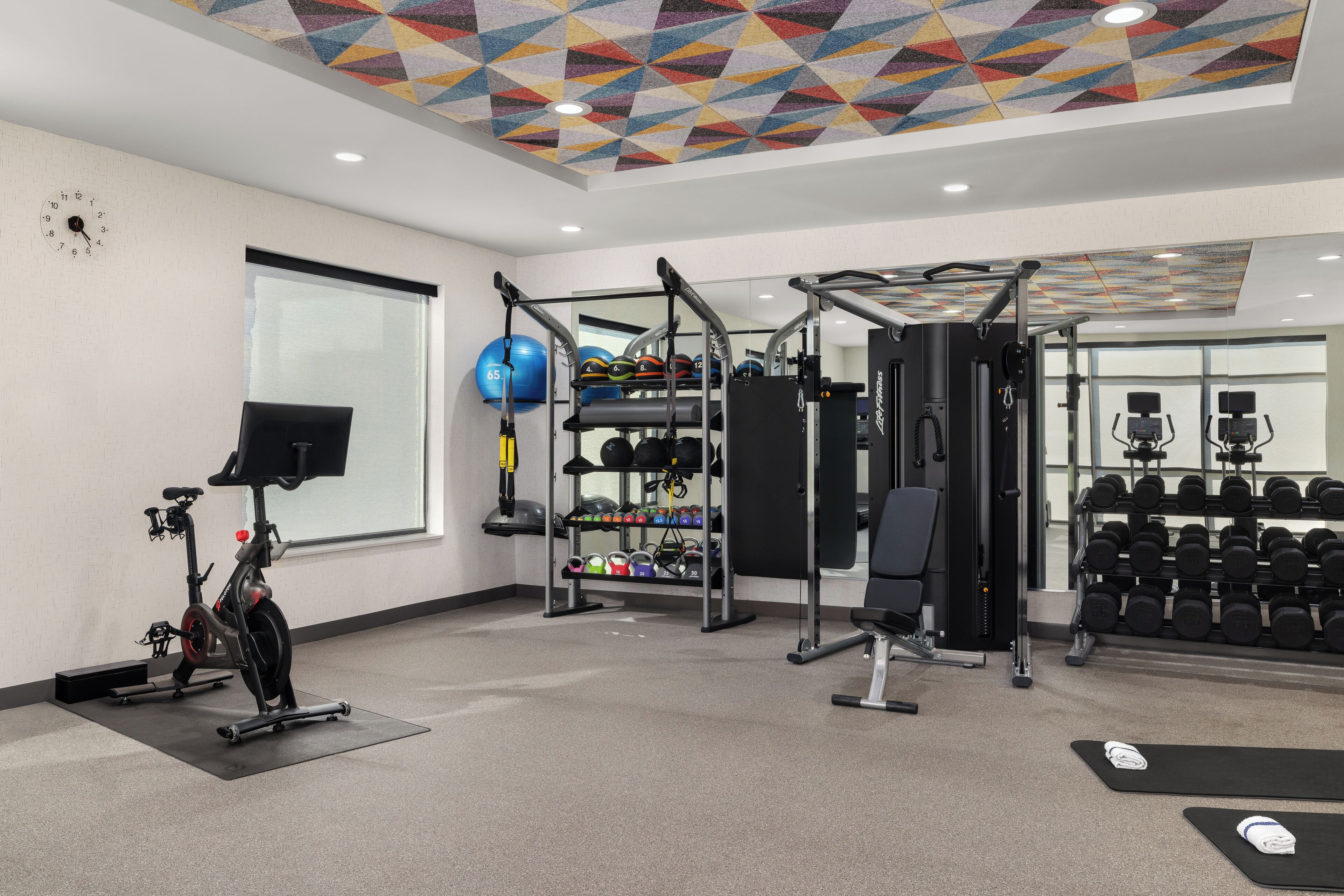A gym with exercise equipment, a wall clock, and a window.