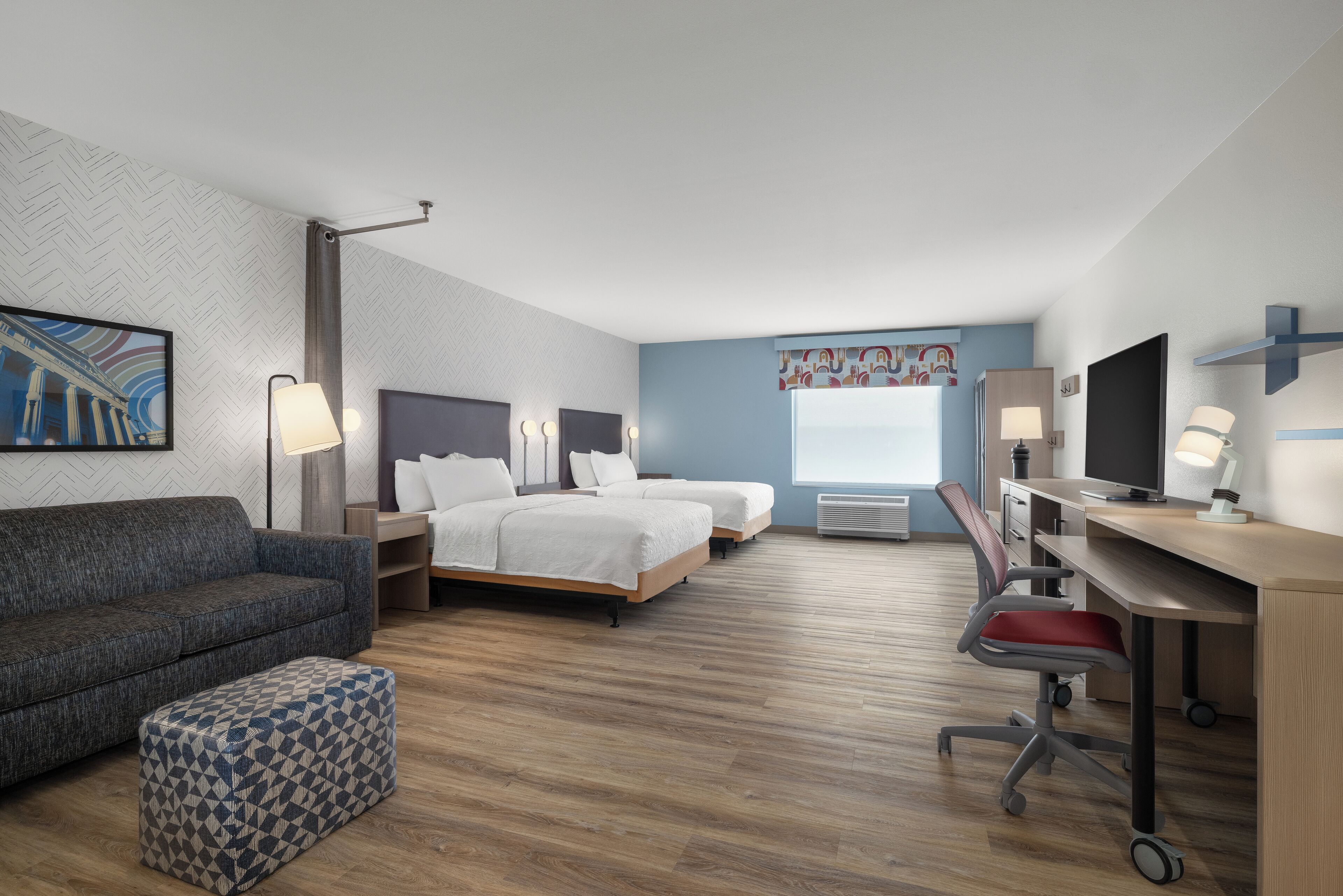 A hotel room with a sofa, two beds, a desk, and a chair.