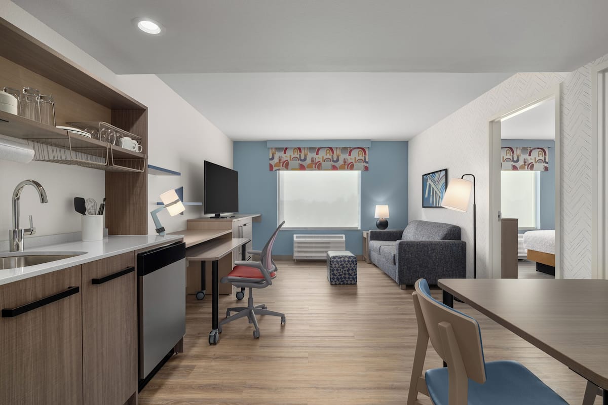 A compact hotel room with a kitchenette, a dining area, a sofa, a bed, and a bathroom.