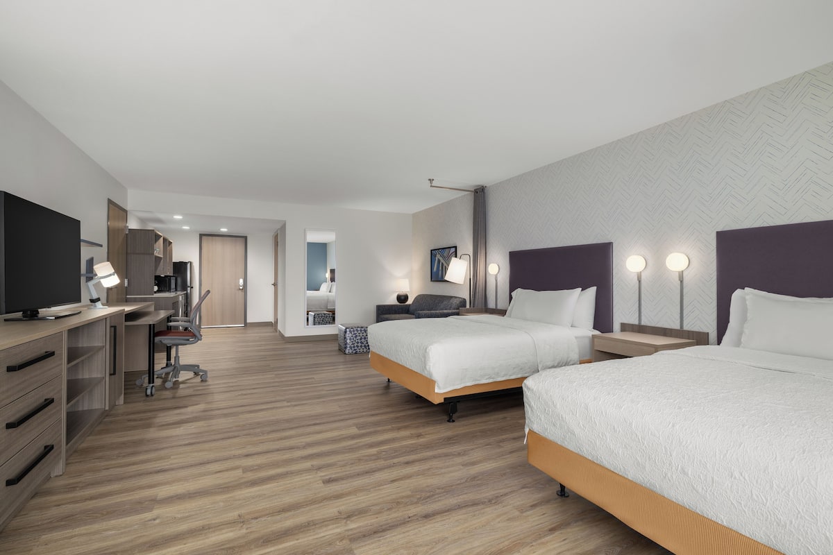 A modern hotel room with two beds, a desk with a computer, a chair, and a television.