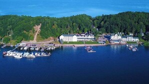A coastal property with a marina, large white buildings, and dense forested hills. - Lakefront 1 bdrm—Pool & Hot Tub—Lake Michigan Access—2 Kayaks Provided! (Onekama)