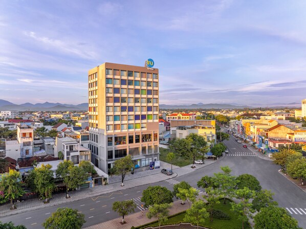 Un hotel moderno con un logo destacado, rodeado por un paisaje urbano y con una vista despejada de las montañas al fondo.