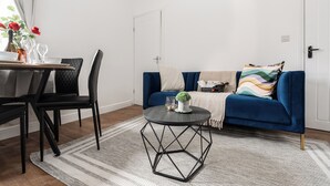 A modern living room with a blue sofa, a round black coffee table, and a dining area with a wooden table and chairs. - Modern 4bedroom City Home Near LFC (Liverpool)