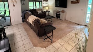 A spacious living area with a large sofa, a coffee table, and a fireplace. There is a television mounted on the wall and a window providing natural light. - Woodson Bend 3 BR Condo 82-4, with  AC, WiFi, Pool, Golf Course, Restaurant (Bronston)