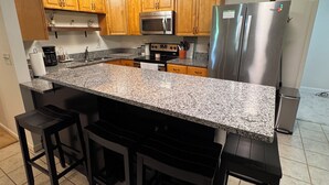 A modern kitchen with granite countertops, wooden cabinets, stainless steel appliances, and black bar stools. - Woodson Bend 3 BR Condo 82-4, with  AC, WiFi, Pool, Golf Course, Restaurant (Bronston)