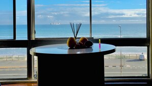 A table with a view of the ocean and a ship in the distance through large windows. - Sea View Zeezicht, Bloubergstrand, Blouberg Beach, Cape Town (Bloubergstrand)
