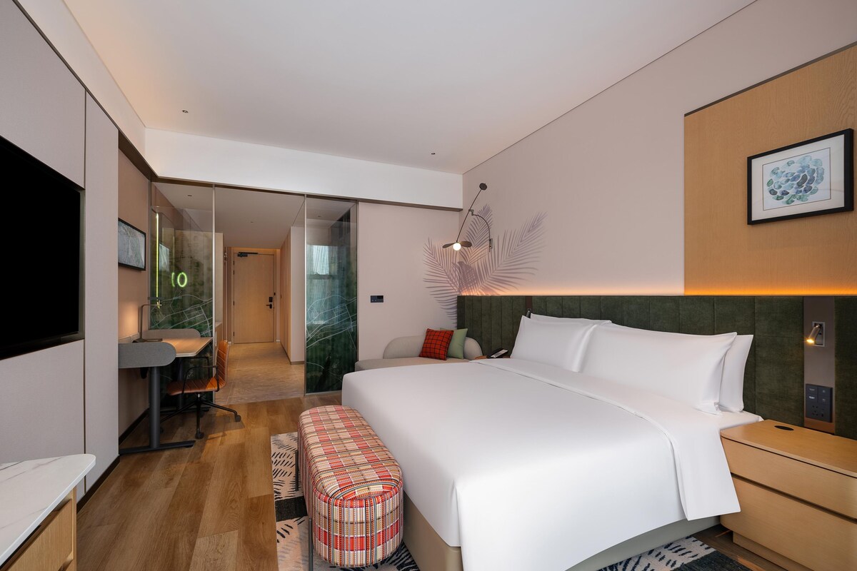 Una habitación de hotel moderna con una cama grande, un escritorio, una silla y un televisor.