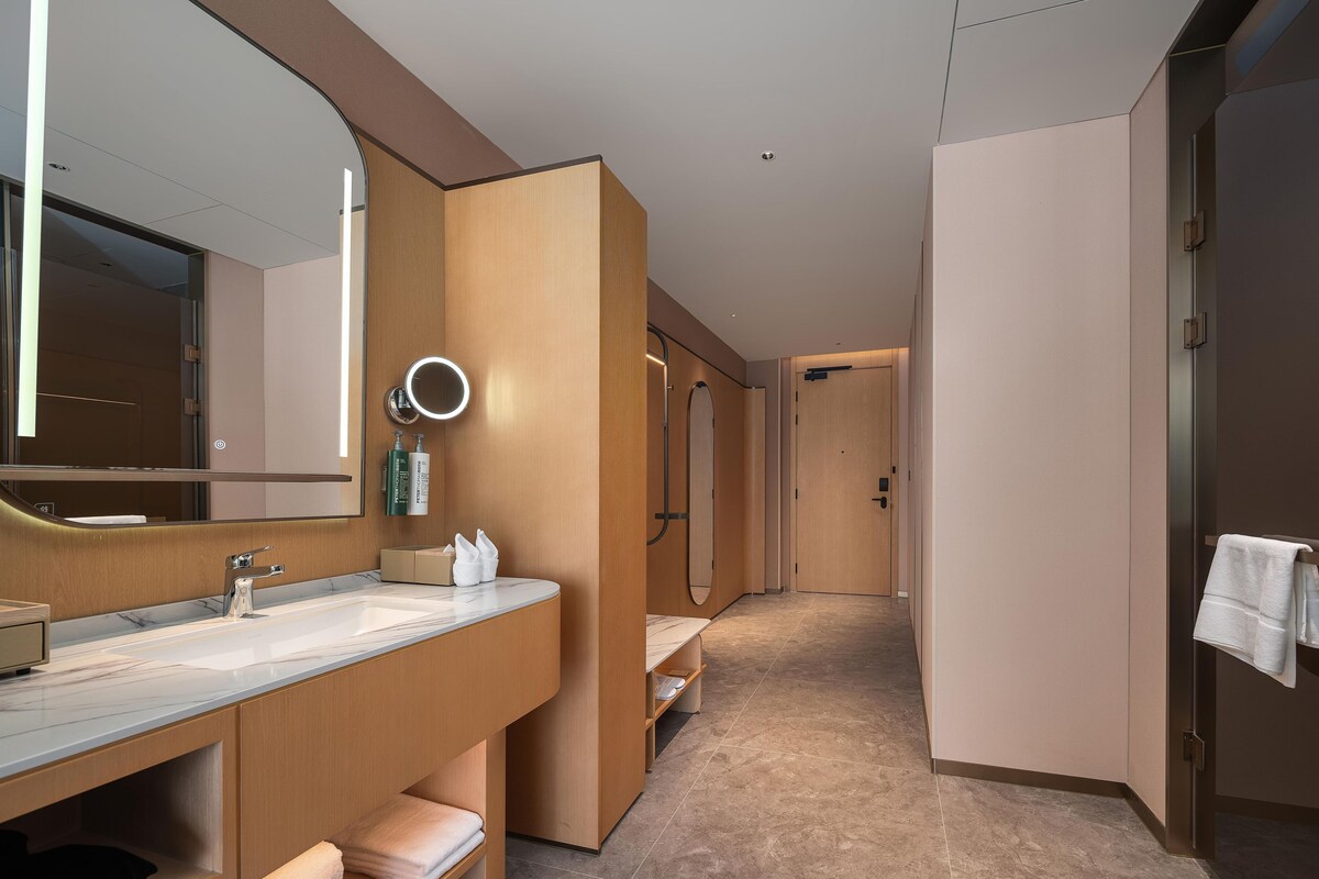 Une salle de bain d’hôtel moderne, dotée d’un grand miroir, d’un lavabo, d’un banc et d’un porte-serviettes.