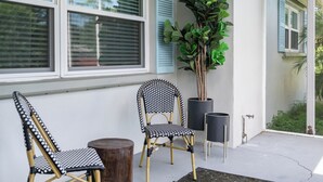 A patio with two wicker chairs, a wooden table, and a potted plant.