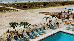 Una piscina con sillas de descanso y palmeras, rodeada por una playa de arena.