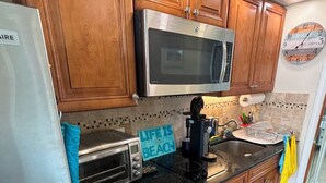 Una cocina con armarios de madera, un refrigerador de acero inoxidable, un microondas, un tostador y un reloj en la pared.
