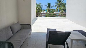 A modern room with a grey sofa, a black chair, and a white table. There is a balcony with a view of palm trees and the ocean. - Departamento en Bahias de Huatulco (Santa Maria Huatulco)