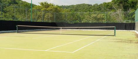 A tennis court with a net, surrounded by a fence and trees.