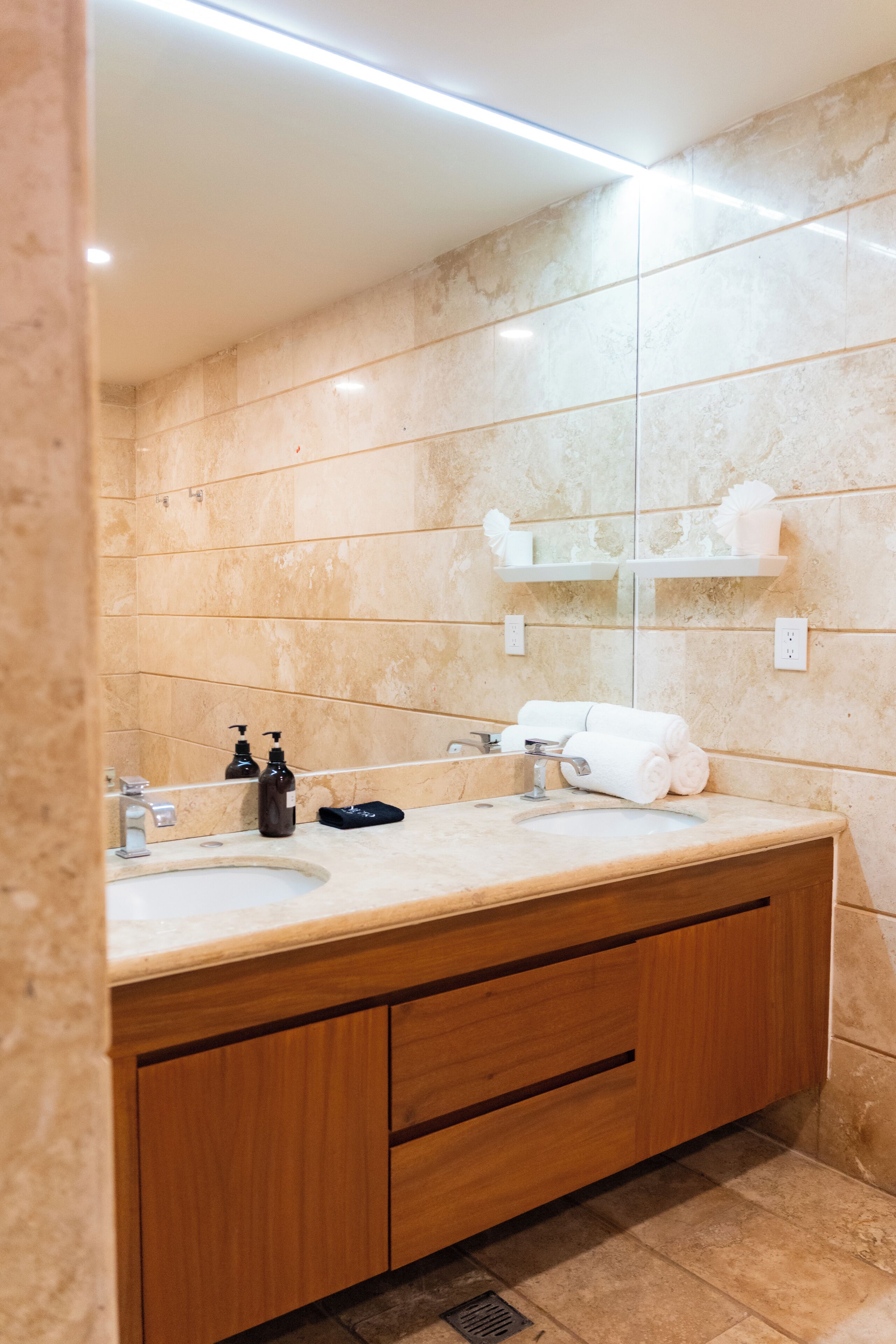A bathroom with a double sink, wooden cabinets, a mirror, and a towel rack.