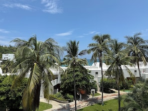 A resort with palm trees, a pathway, and a view of the ocean. - Departamento en Bahias de Huatulco (Santa Maria Huatulco)