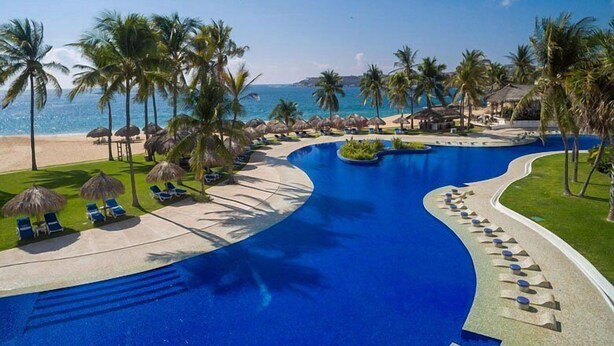 A resort with a large swimming pool, palm trees, and a beach. - Departamento en Bahias de Huatulco (Santa Maria Huatulco)