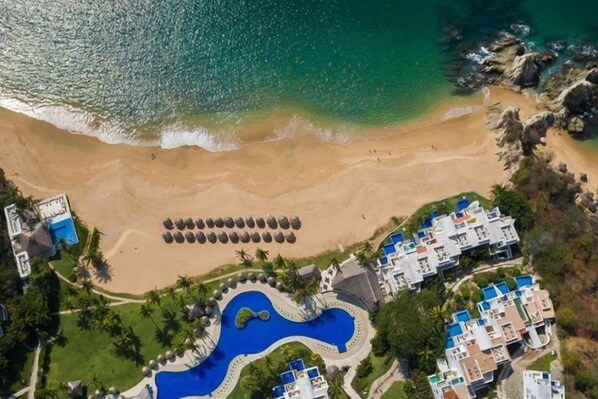 Luchtbeeld van een resort met een strand, een zwembad en verschillende gebouwen.