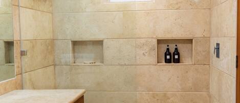 A bathroom with a large mirror, a wooden vanity, a shower area with a glass door, and a small window.