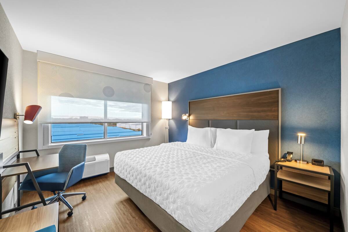 Een hotelkamer met een groot bed, een bureau, een stoel, een nachtkastje, een lamp en een raam met uitzicht.