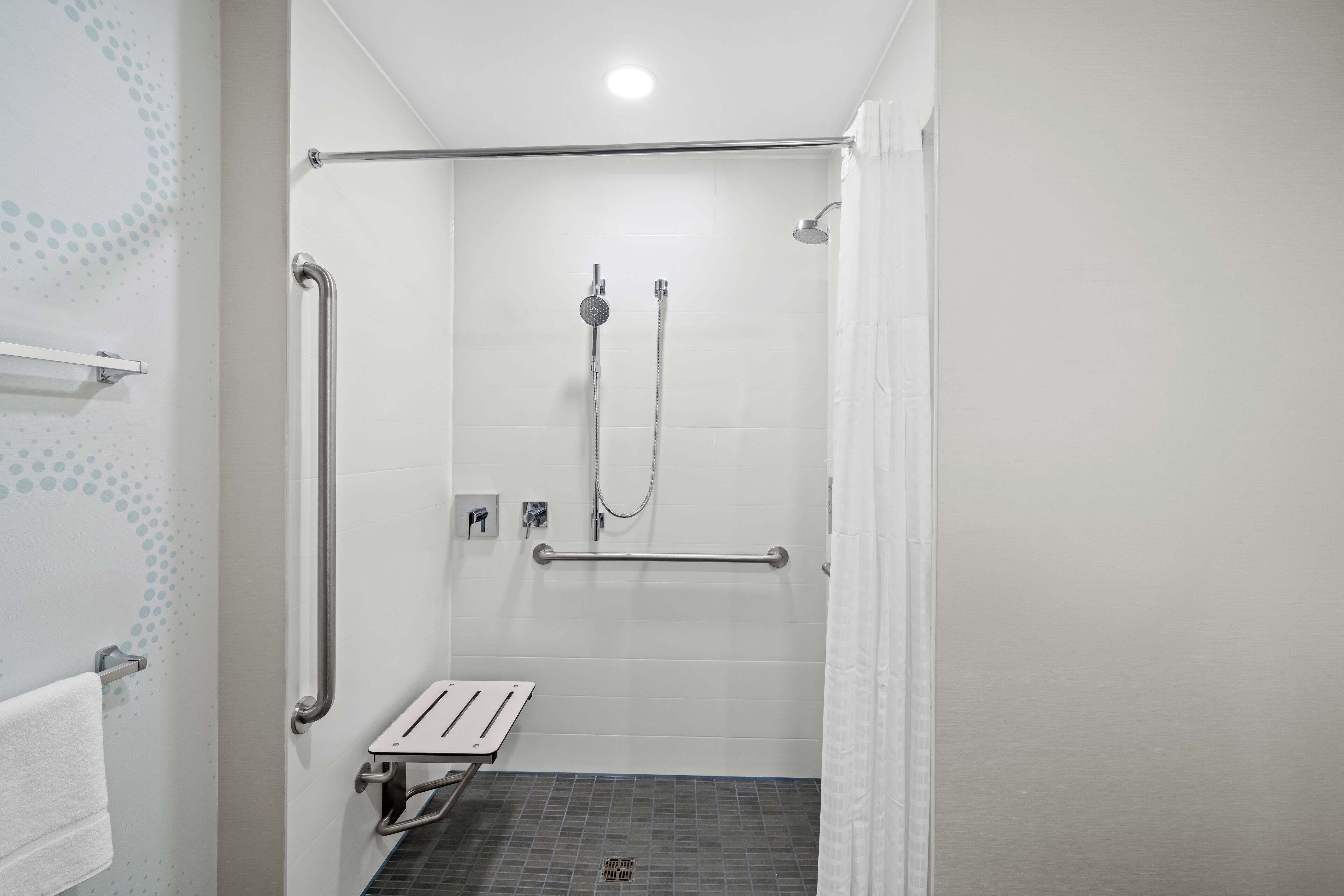 Un espace douche équipé d’une barre d’appui, d’un pommeau de douche à main et d’un drain au sol.