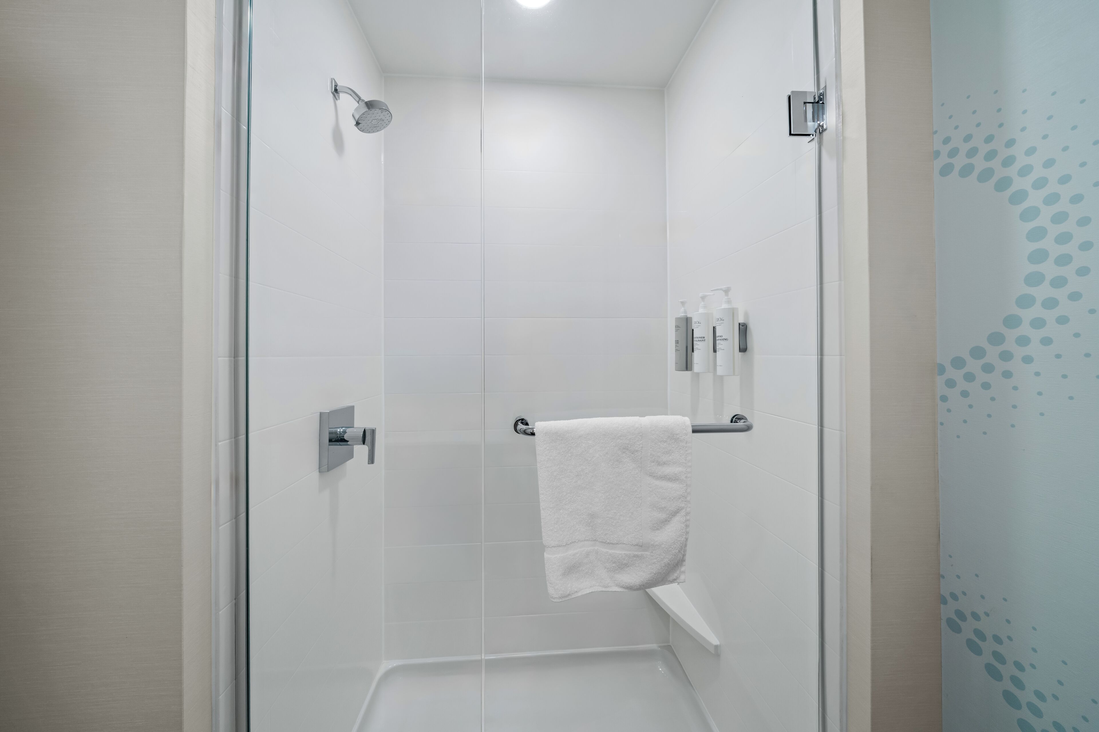 A modern shower with a glass door, a white towel hanging on a rack, and toiletries on a shelf.