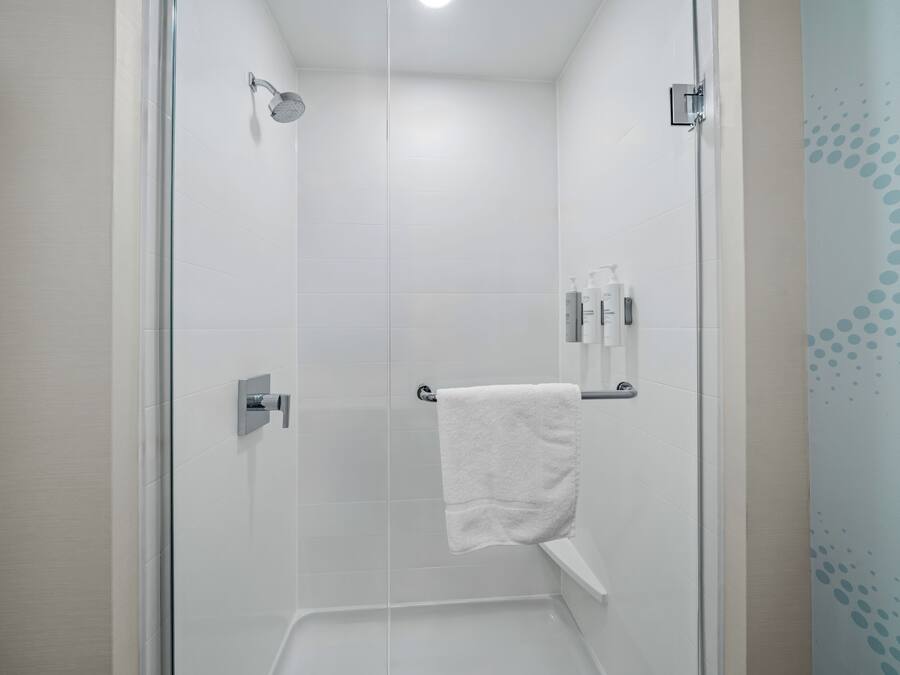 A modern shower with a glass door, a white towel hanging on a rack, and toiletries on a shelf.