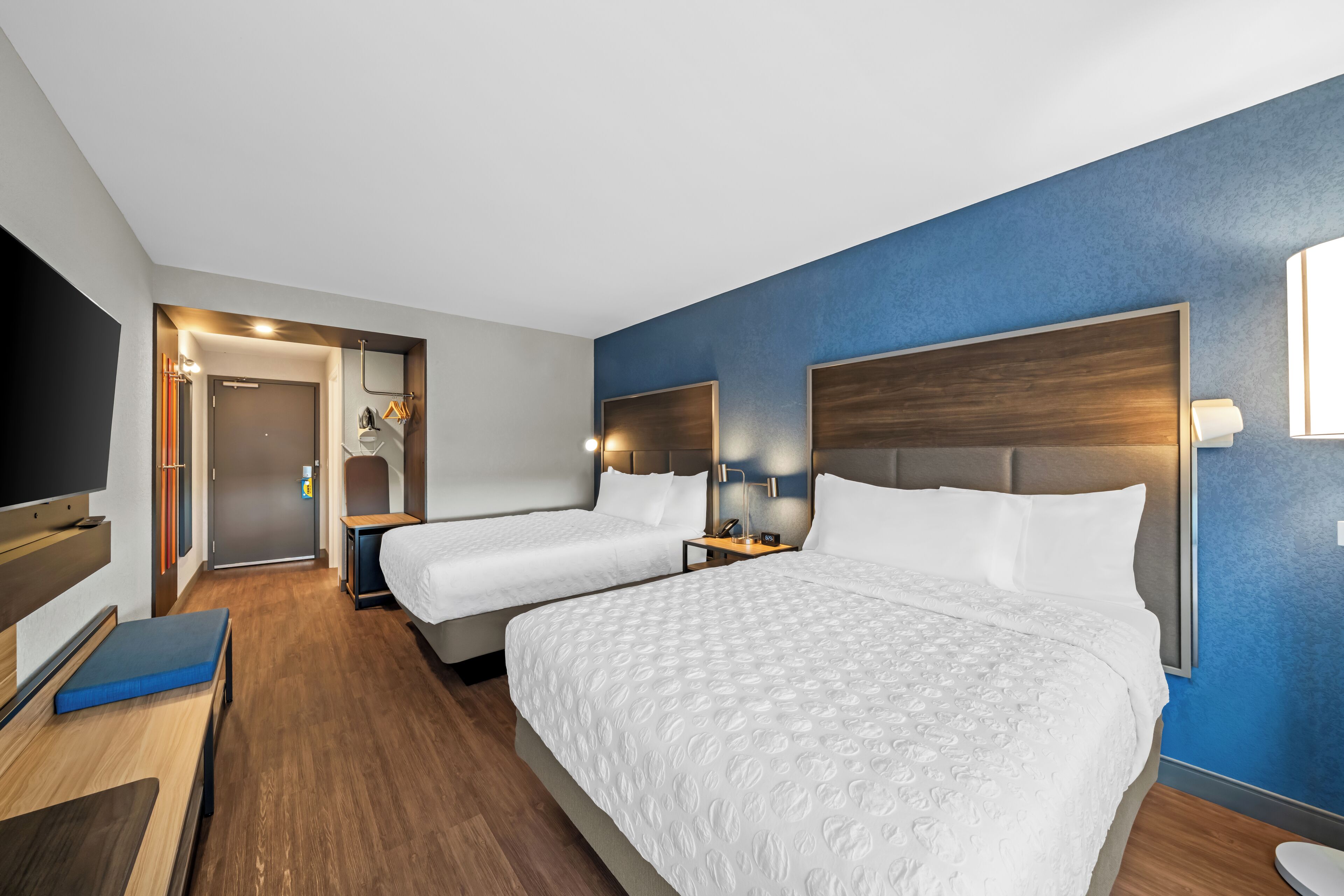 Habitación de hotel con dos camas, televisión, escritorio y baño visible a través de una puerta abierta.