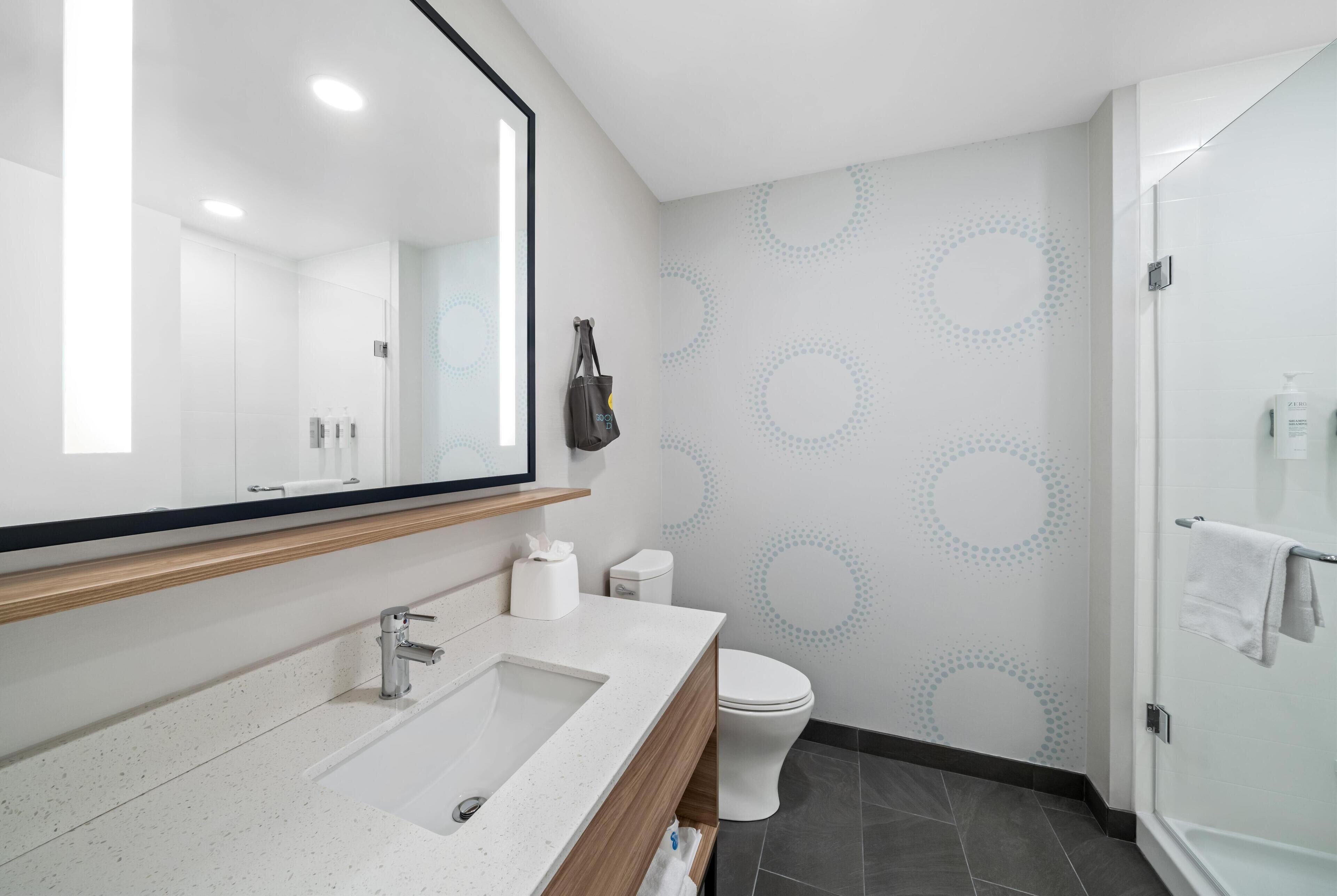 Un baño moderno con un espejo grande, un lavamanos, un inodoro y una zona de ducha.