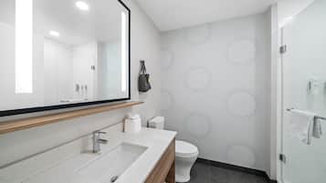 Un baño moderno con un espejo grande, un lavamanos, un inodoro y una zona de ducha.