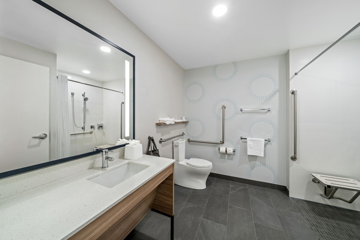 Un baño moderno con un espejo grande, lavamanos, inodoro y ducha.