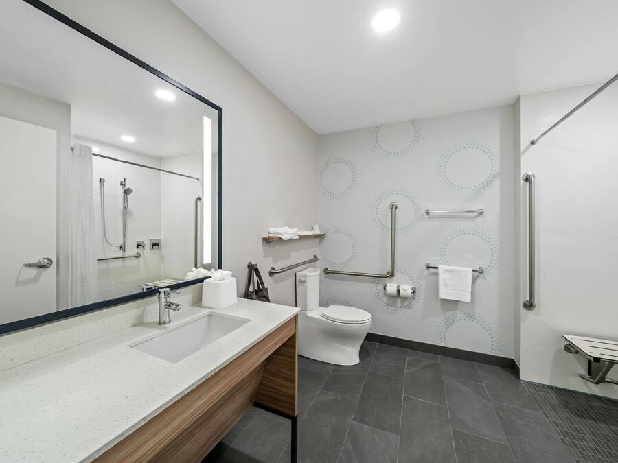 A modern bathroom with a large mirror, a sink, a toilet, and a shower area.