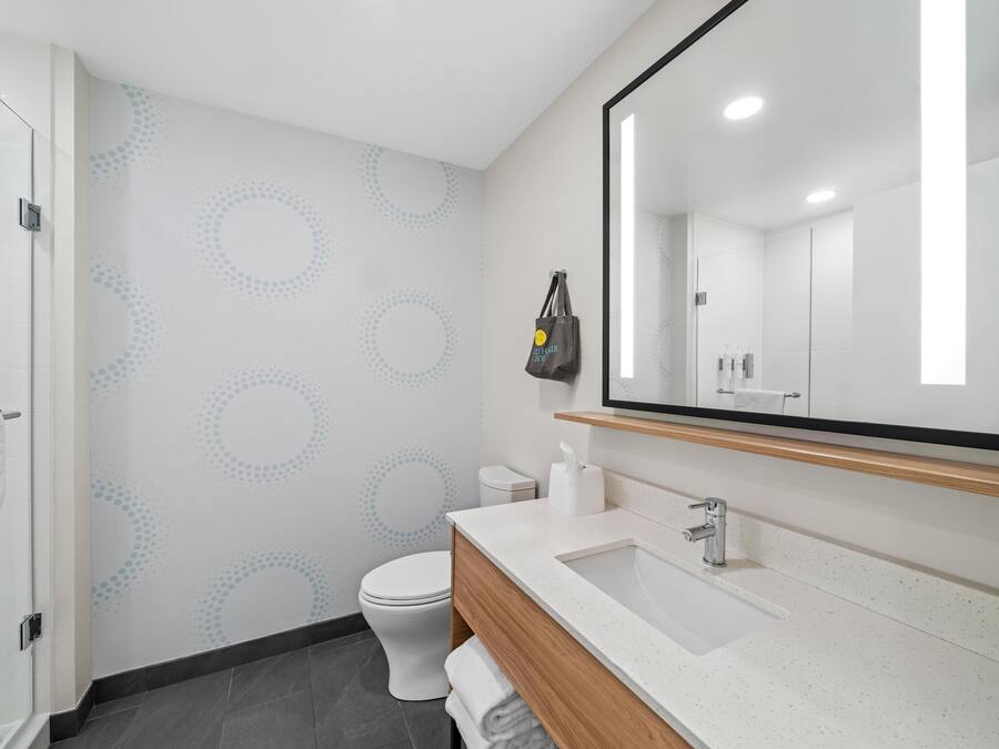 A modern bathroom with a large mirror, white sink, and toilet.