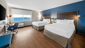 Une chambre d’hôtel avec deux lits, un bureau, une chaise et une grande fenêtre donnant sur la mer.