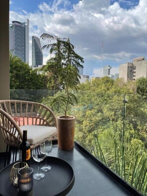 A balcony with a wicker chair, a potted plant, and a table with wine glasses and a bottle. - Condesa Cibel  (Mexico City)