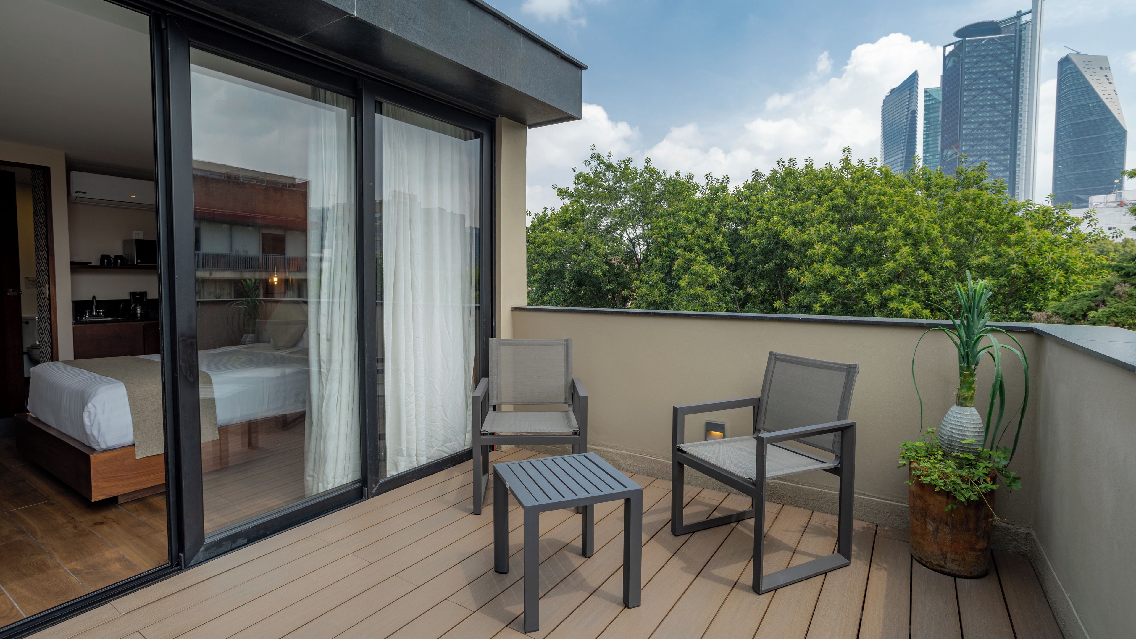 A balcony with a bed, two chairs, a small table, and a potted plant.