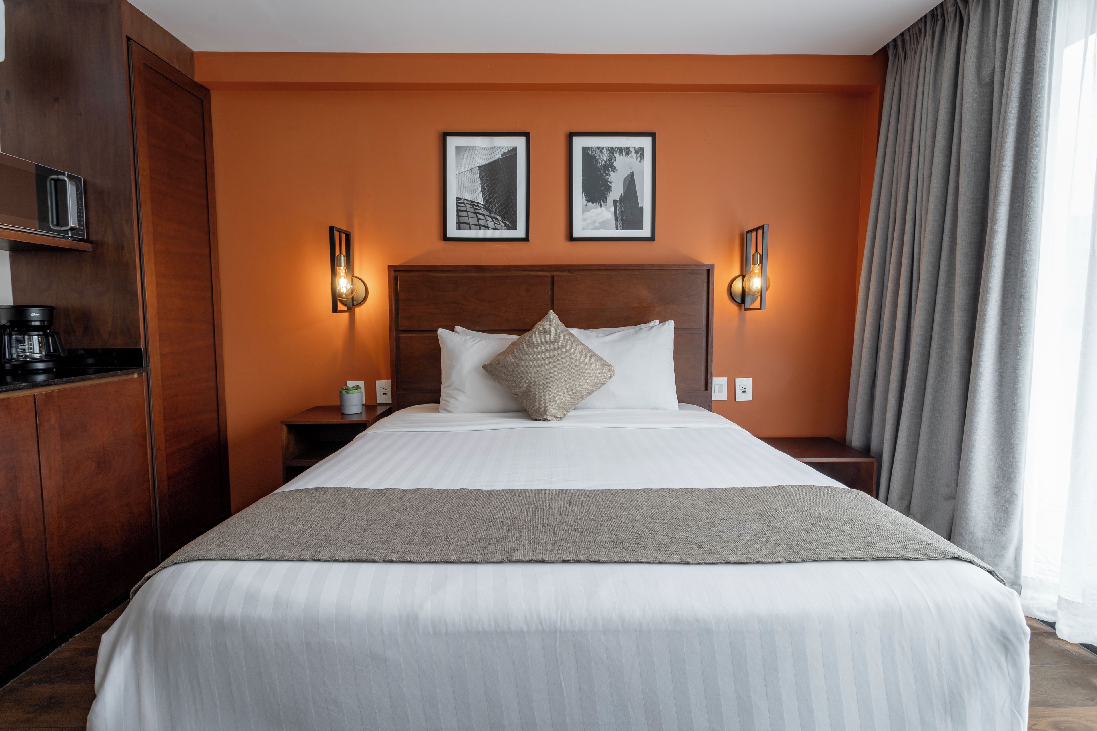A hotel room with a large bed, two wall-mounted light fixtures, a coffee machine, and a small table with a plant.
